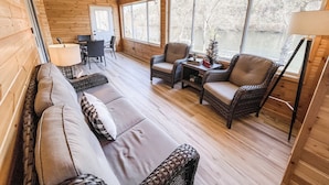 Houten chalet interieur met een bank, stoelen, een eettafel en uitzicht op een meer.
