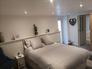 A bedroom with a large bed, a nightstand, a chair, a potted plant, and a heart-shaped mirror on the wall. - High Gables Apartment 1, goodrington beach (Paignton)