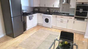 Une cuisine moderne avec des meubles blancs, un réfrigérateur en acier inoxydable, un lave-linge et un four Bosch.