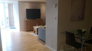 Un vaste espace de vie doté d’un plancher en bois, d’une table à manger en verre et d’un téléviseur à écran plat fixé au mur.