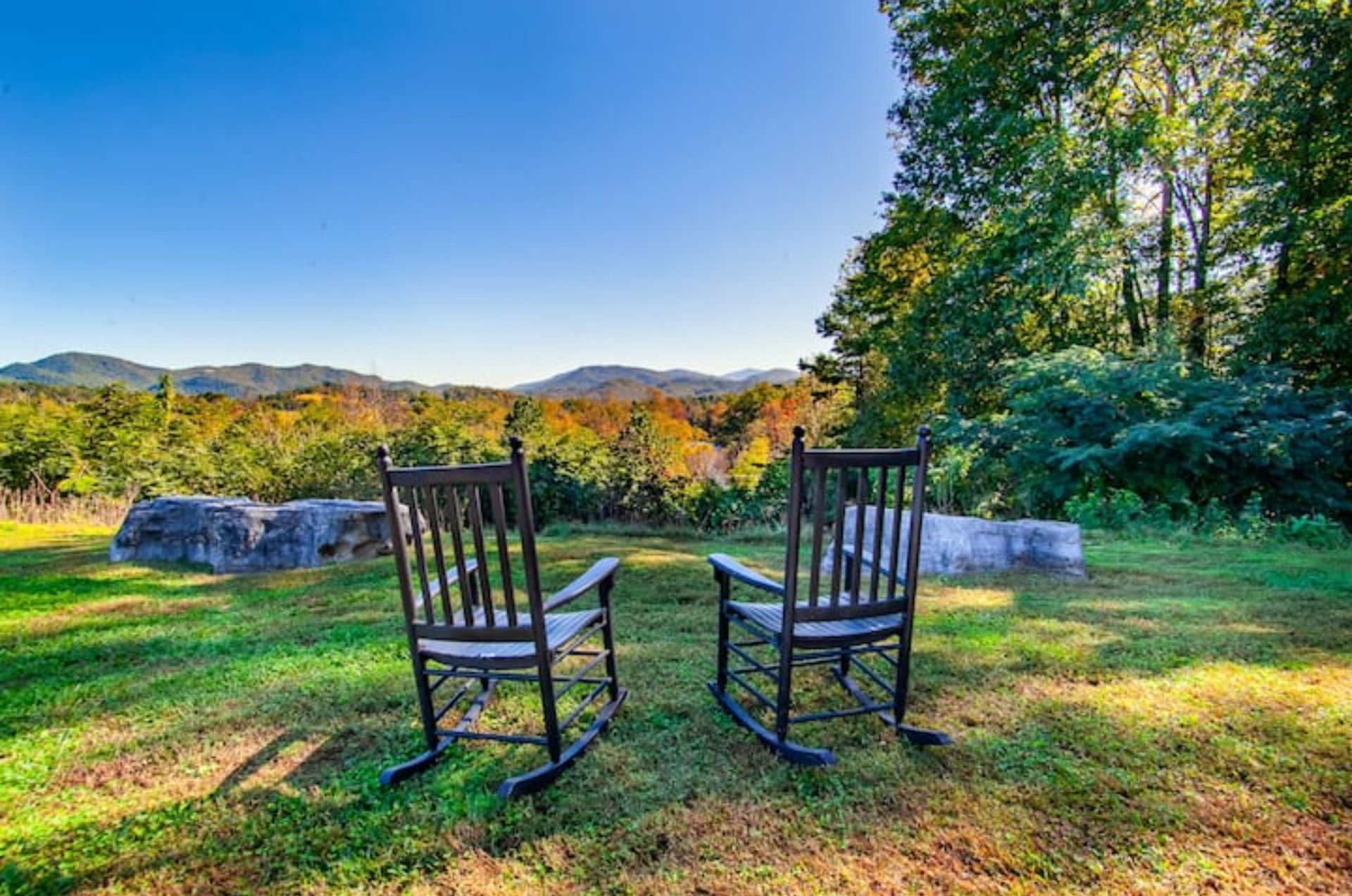 Two rocking chairs facing a scenic view of a forest with mountains in the background.