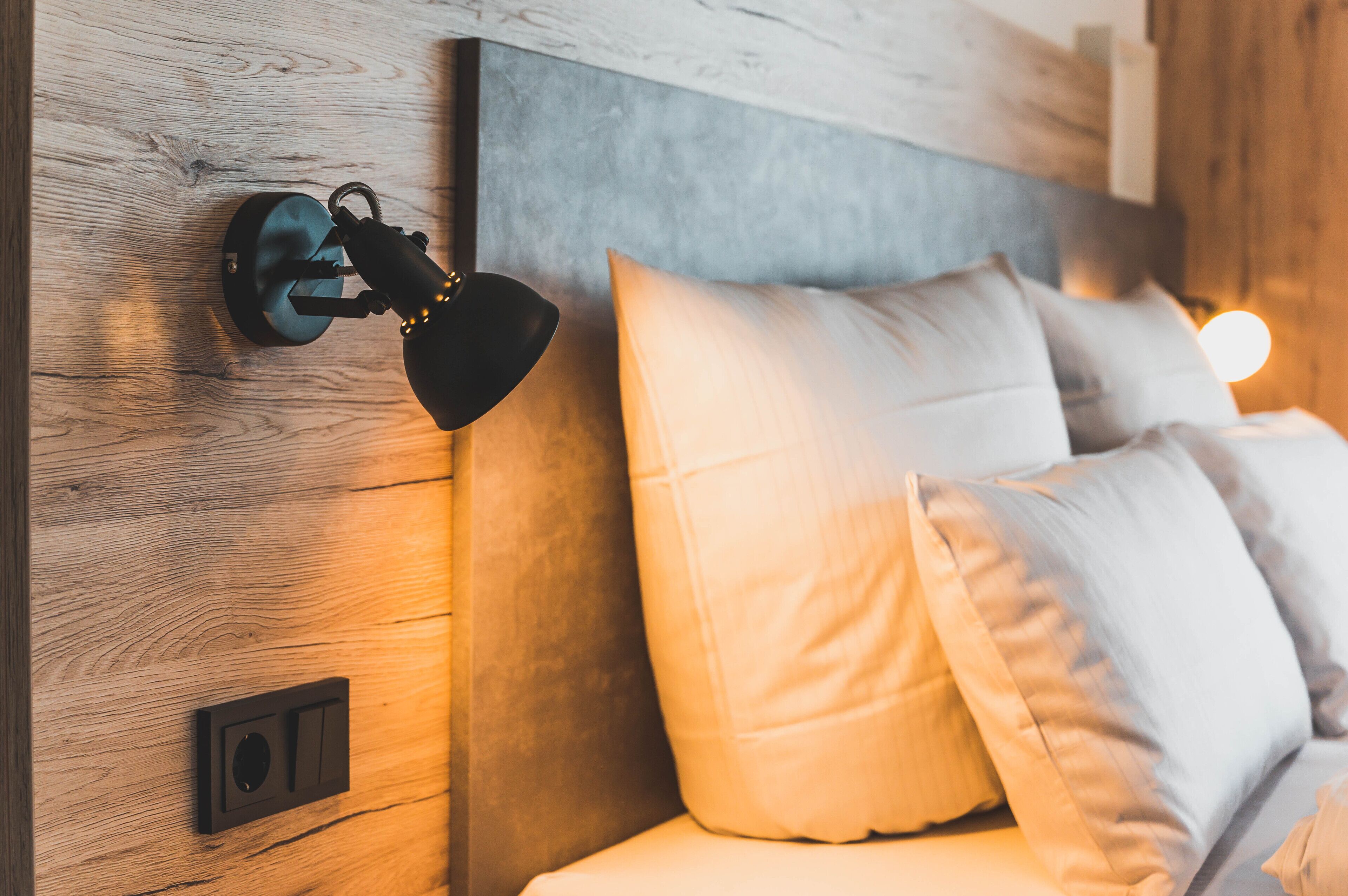 Une chambre à coucher moderne avec une tête de lit en bois, une lampe fixée au mur et un lit recouvert de linge de lit blanc.