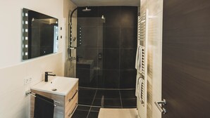 Ein modernes Badezimmer mit Waschtisch, Spiegel, Dusche und Handtuchhalter.
