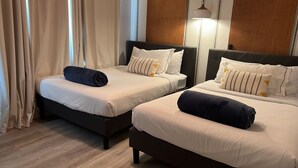 Duas camas de solteiro com cabeceiras escuras e roupa de cama branca, piso de madeira e um abajur na parede.