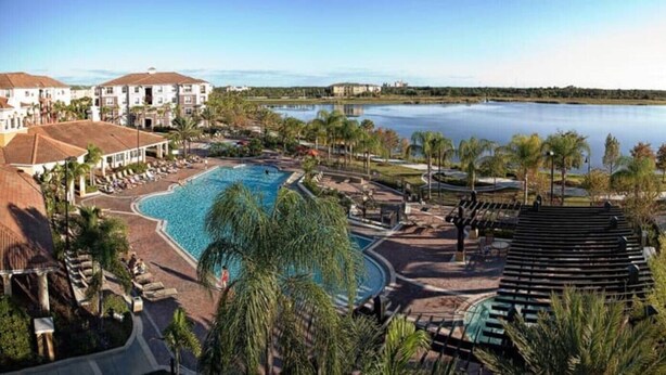 Um resort com uma piscina grande, palmeiras e vista para um lago.