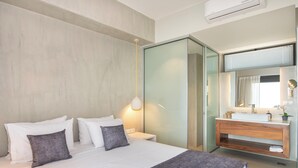 A modern hotel room with a large bed, a bedside table, a built-in vanity with a mirror, and a sliding glass door leading to a bathroom. - Porti Iraklis 4 - A Stylish Eco Villa near beaches (Rethymno)