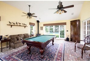 Relax in this inviting room with a pool table, sofa, and large windows offering a view of the outdoors.