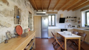 A rustic kitchen with wooden beams, a built-in refrigerator, and a dining area with a wooden table and chairs. - Dolly's Dream House (Patmos)