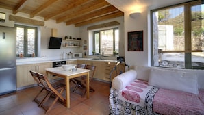 A cozy kitchen with wooden beams, a dining area with a table and chairs, and a sofa with a patterned throw. - Dolly's Dream House (Patmos)