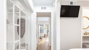 Un dormitorio con una cama, un televisor montado en la pared y un vestidor con estantes y un bolso para colgar.
