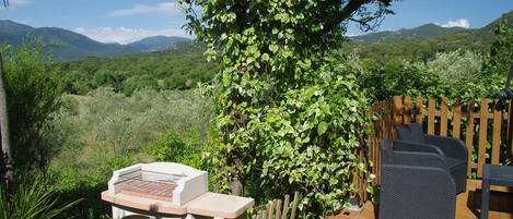 An outdoor patio with a grill, wicker furniture, and a view of a lush landscape with mountains.