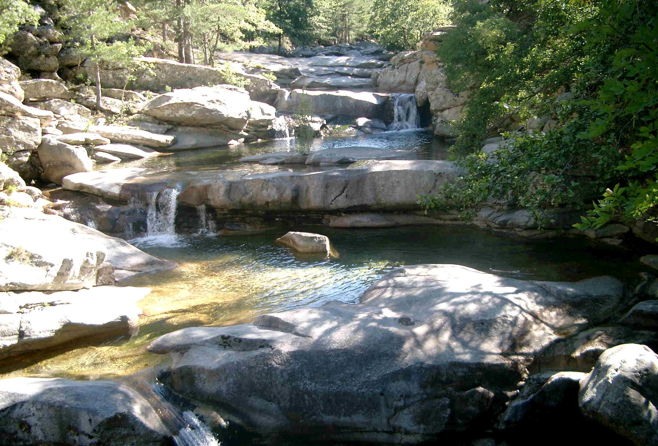 A natural rocky landscape with a small waterfall and clear water.