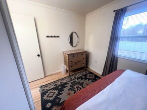 Un dormitorio con cama, cómoda, espejo y alfombra estampada.