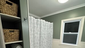 A bathroom with a toilet, a green rug, a shower curtain, and shelves with towels. - Little Bass Cabin - Kayaks & Clear Water Swimming (Grand Rapids)