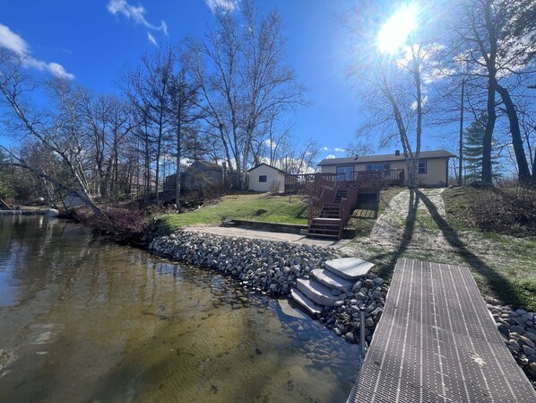 A residential area with a clear pond, wooden deck, stone steps, and houses with a staircase leading to a deck.