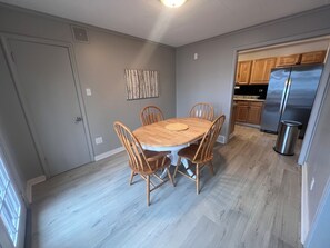 Un comedor con una mesa y sillas de madera, una cocina con armarios de madera y un refrigerador de acero inoxidable, y un piso de tono claro.