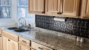 A kitchen with wooden cabinets, a granite countertop, a black backsplash, and a window with a view of trees. - Little Bass Cabin - Kayaks & Clear Water Swimming (Grand Rapids)