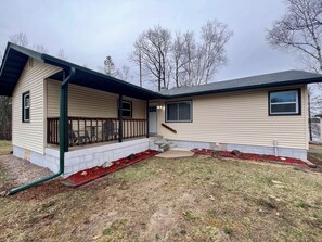 A single-story house with a covered porch, a front door, and a small front yard with red mulch and rocks. - Little Bass Cabin - Kayaks & Clear Water Swimming (Grand Rapids)