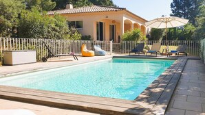 Ein rechteckiger Pool mit gefliestem Deck, umgeben von einem weißen Zaun. In der Nähe des Pools befinden sich Liegestühle und ein Sonnenschirm.