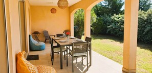 Uma área de refeições ao ar livre com uma mesa posta para quatro pessoas, rodeada por cadeiras e um puff.