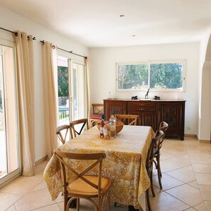 Uma sala de jantar com uma mesa posta para quatro pessoas, um armário de madeira e uma janela com vista para árvores.