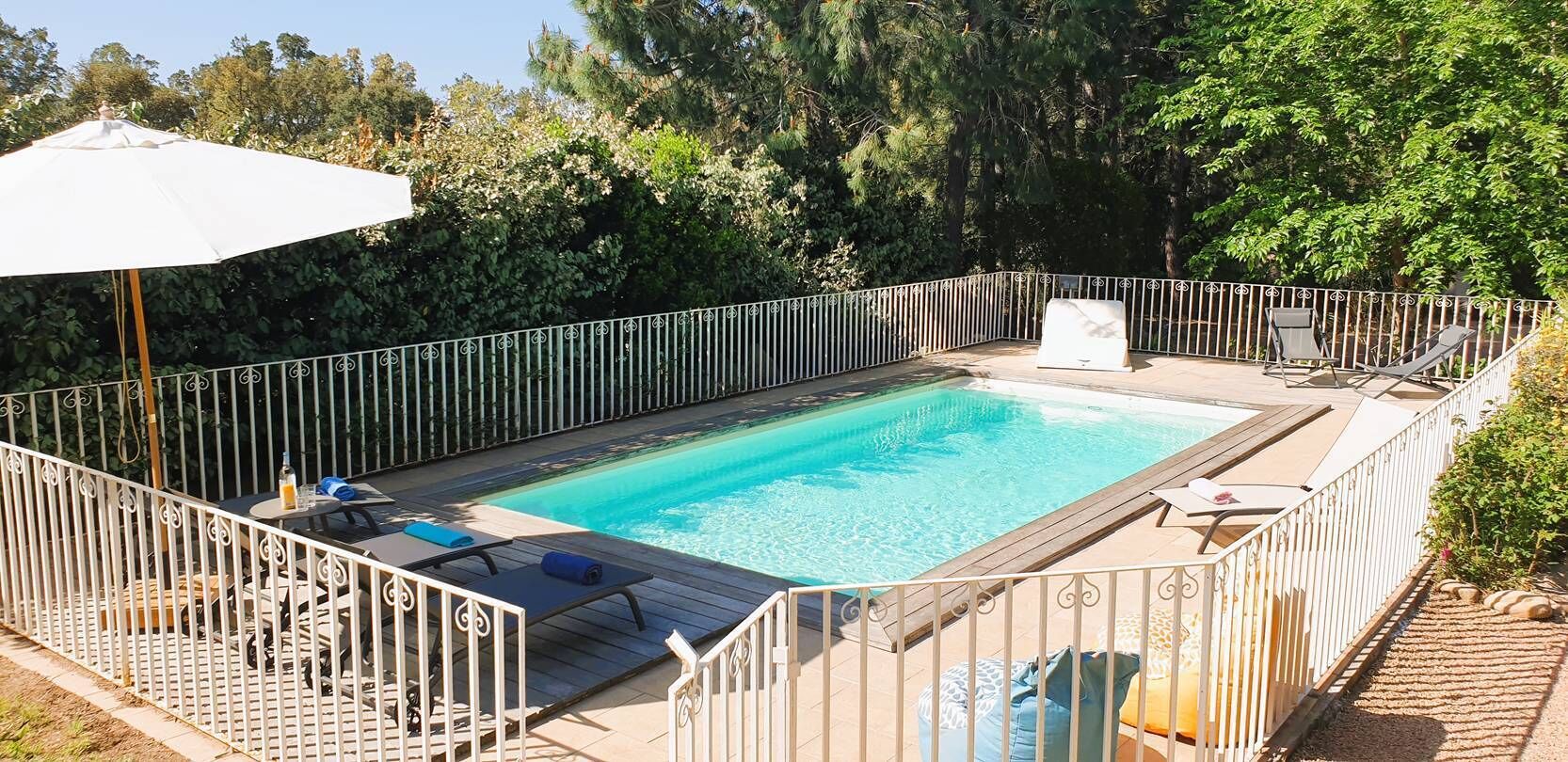 Ein rechteckiger Pool mit Holzterrasse, umgeben von einem weißen Metallzaun.