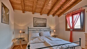 Quarto com teto de madeira, cama com roupa de cama florida, duas mesas de cabeceira com luminárias e uma janela com cortina.