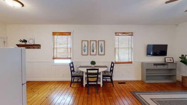A dining area with a wooden table and chairs, flanked by two windows with blinds. - Beach Access to Ozark, Visit the Cottage on Valley Road! (Osage Beach)