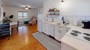 A modern kitchen with white cabinets, a microwave, and a stove. There is a dining area with a table and chairs, and a living room with a sofa and a coffee table. - Beach Access to Ozark, Visit the Cottage on Valley Road! (Osage Beach)