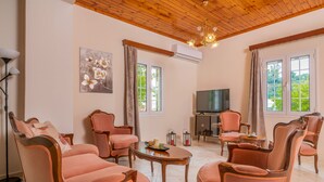 A spacious living room with a wooden ceiling, large windows, and a flat-screen TV. - Avrochares Villa (Ζάκυνθος)