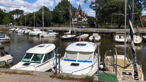 A marina with several boats docked, a building with a pointed roof in the background, and a clear sky. - Villa Ferry (Andernos-les-Bains)