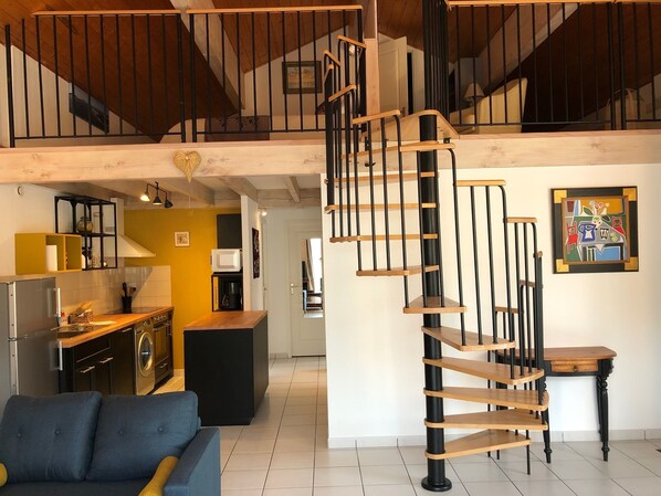 A spacious living area with a modern staircase, a kitchen with yellow walls, and a dining area with a table and chairs.
