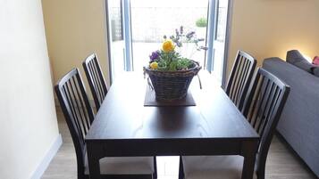 Een eettafel met stoelen, een bloemenmand en een uitzicht door een open deur.