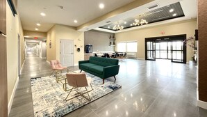 A spacious lobby with a green sofa, a pink chair, and a patterned rug. - Palace Inn Blue Houston East Beltway 8 (Houston)