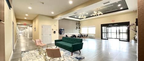 A spacious lobby with a green sofa, a pink chair, and a patterned rug.