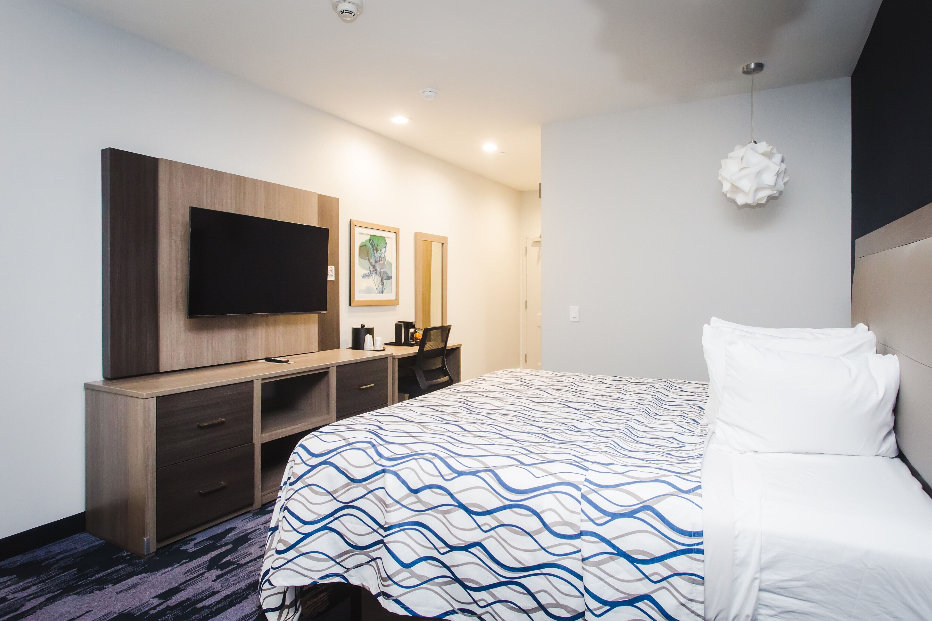 Una habitación de hotel con una cama grande, un televisor de pantalla plana, un escritorio con silla y una obra de arte colgada en la pared.