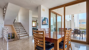 Un'ampia sala da pranzo con un grande tavolo di legno e sedie, una scala e vista su un patio esterno attraverso porte in vetro.