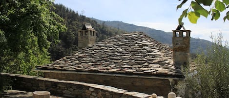 A stone-roofed building with a stone wall and a wooden post in the foreground.