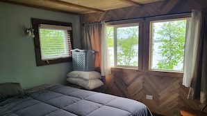 A bedroom with a bed, a wooden herringbone wall, a window with curtains, and a wooden rocking chair.