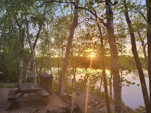 A wooden picnic table and bench near a body of water, surrounded by trees. - The Blue Loon Cabin and pontoon in Northern wi (Lake Nebagamon)