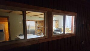 A room with wooden walls and a window overlooking a kitchen area.