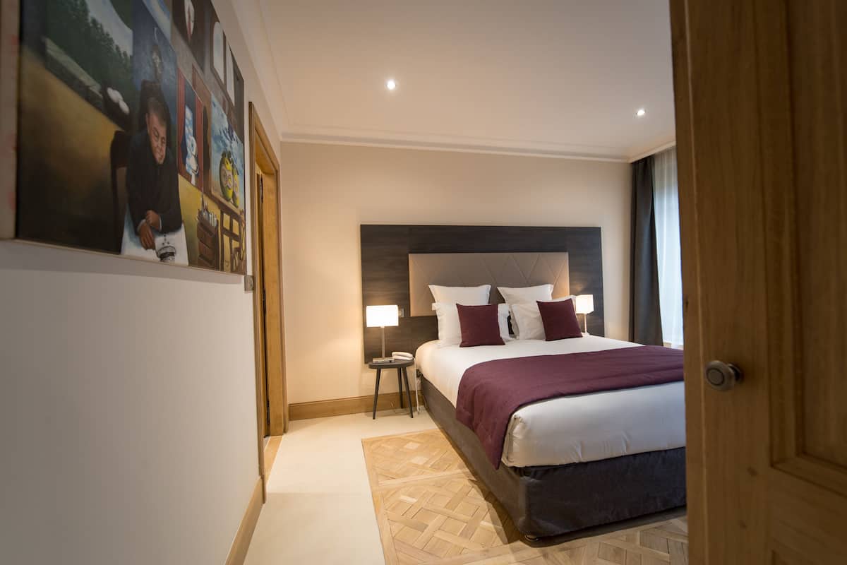 Ein Hotelzimmer mit einem großen Bett, einem Nachttisch, einer Wandleuchte und einem gemusterten Teppich.