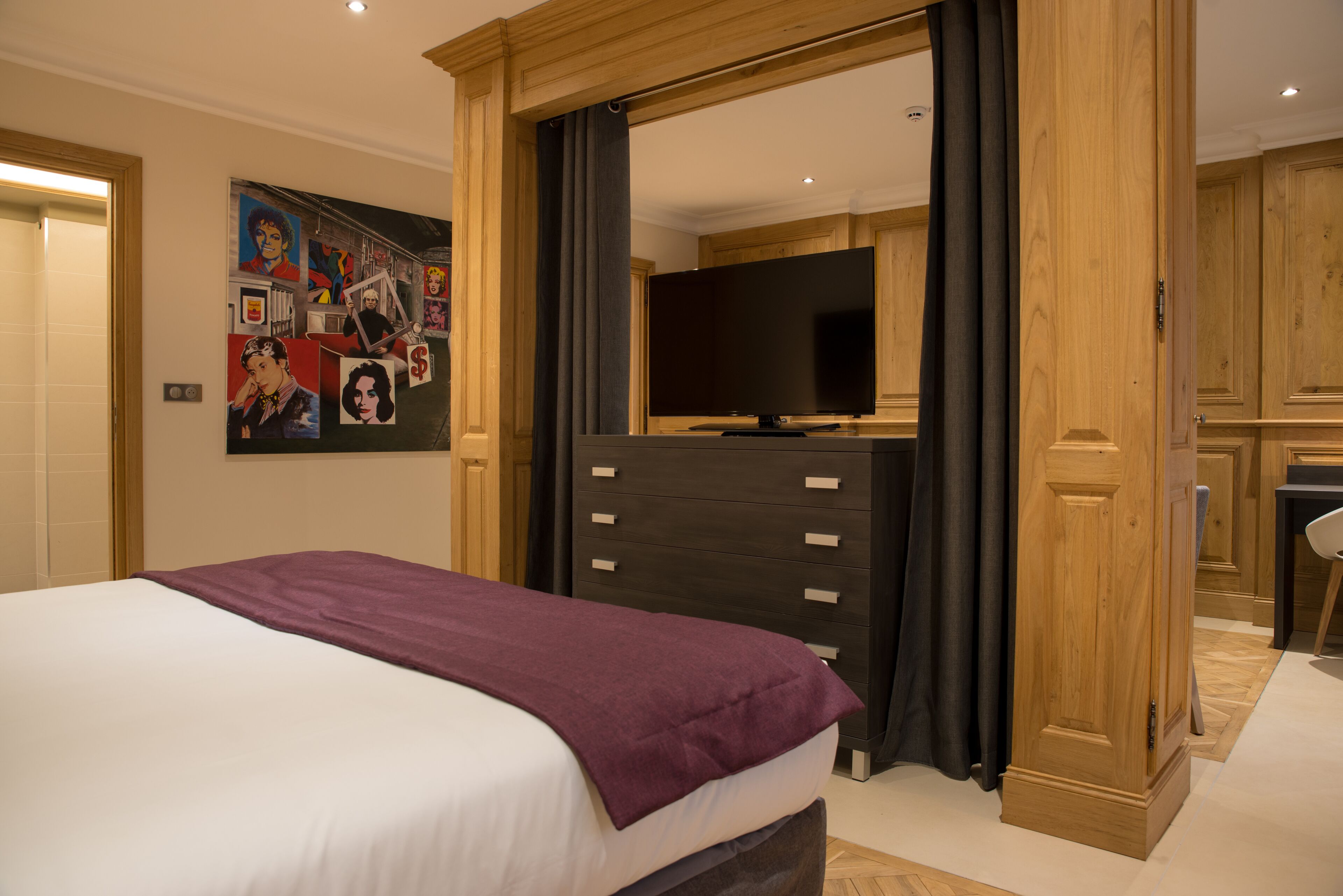 Habitación de hotel con una cama grande, un aparador, un televisor y una pared decorada con obras de arte.