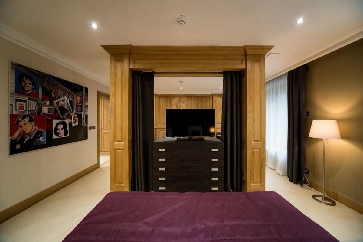 Ein Hotelzimmer mit einem großen Bett, einem Fernseher, einer Holztür und einem Bild an der Wand.