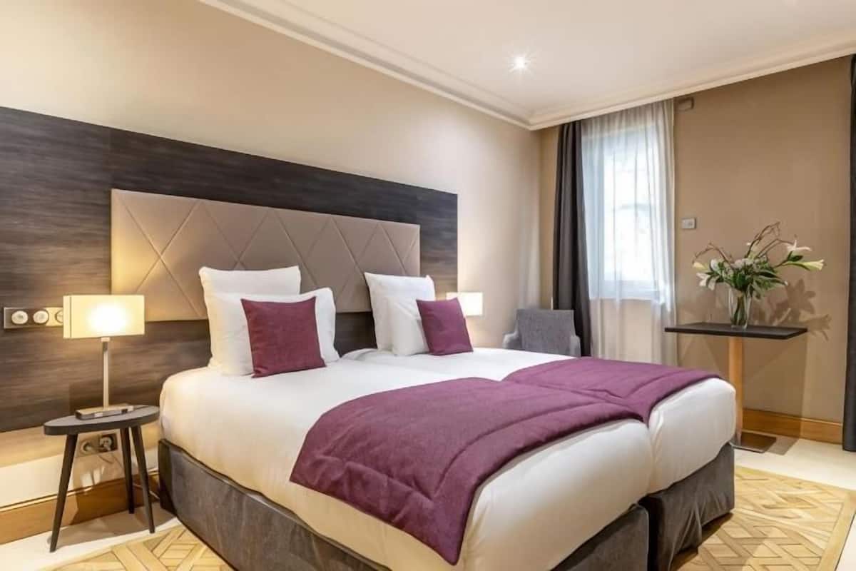 Ein Hotelzimmer mit einem großen Bett, einem Nachttisch mit Lampe, einem Beistelltisch und einer Vase mit Blumen.