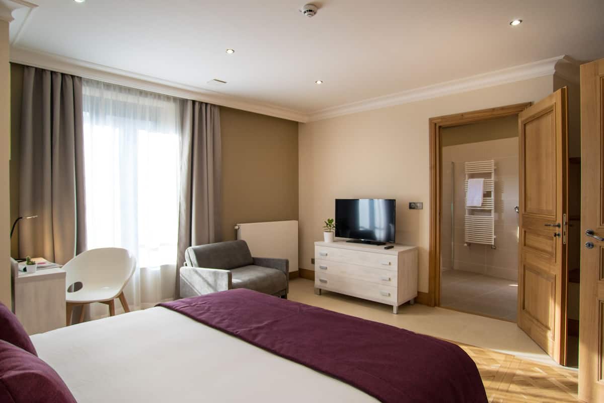 Ein modernes Hotelzimmer mit einem großen Bett, einem Fernseher, einem Schreibtisch mit Stuhl und einem Kleiderschrank.