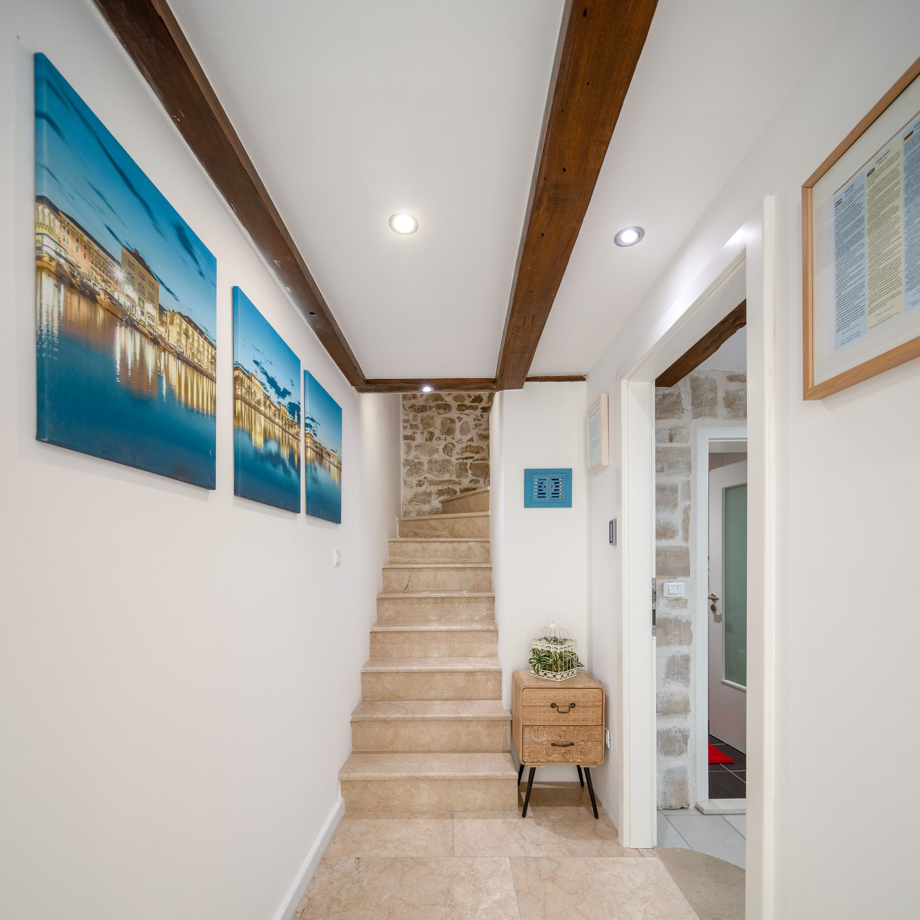 A staircase leading to a landing with a stone wall, a wooden cabinet, and three framed pictures on the wall.