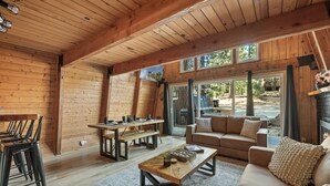 A cozy cabin interior with wooden walls, a dining area, a sofa, and a fireplace.