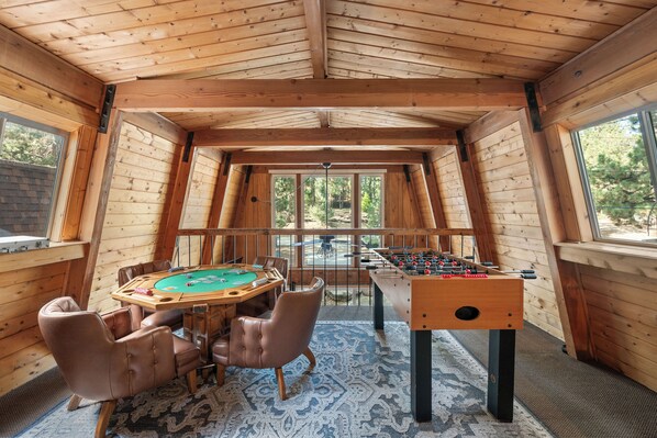 Una habitación con piso de madera, mesa de billar, sillones de cuero y mesa de fútbol.