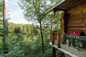 A wooden cabin with a deck overlooking a forested area and a lake.